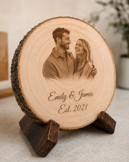 Close up of a custom laser engraved couple portrait on a natural wood slice with visible wood grain and bark edge.